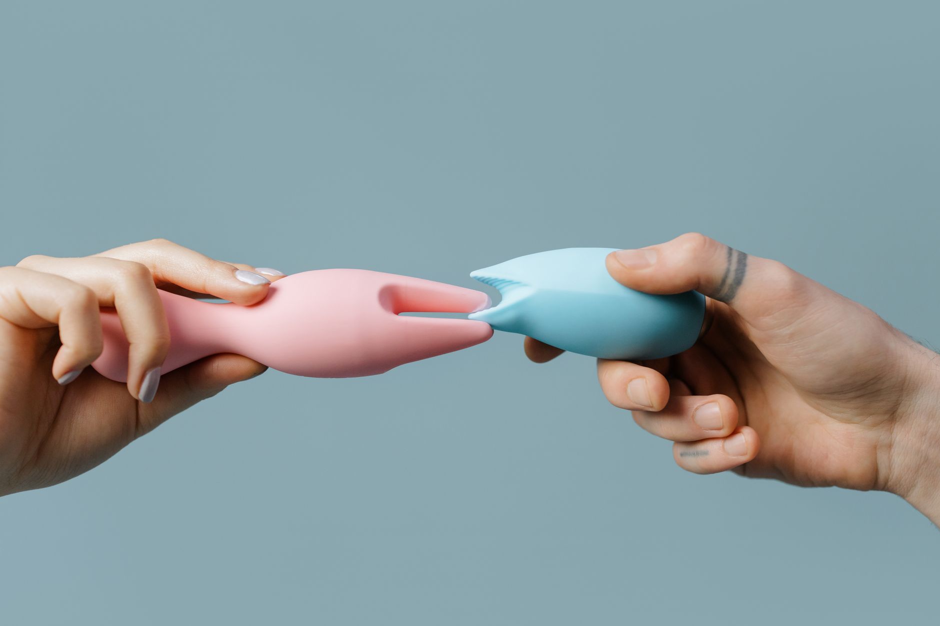 Close-up of hands holding multiple silicone clitoral vibrators in soft pastels