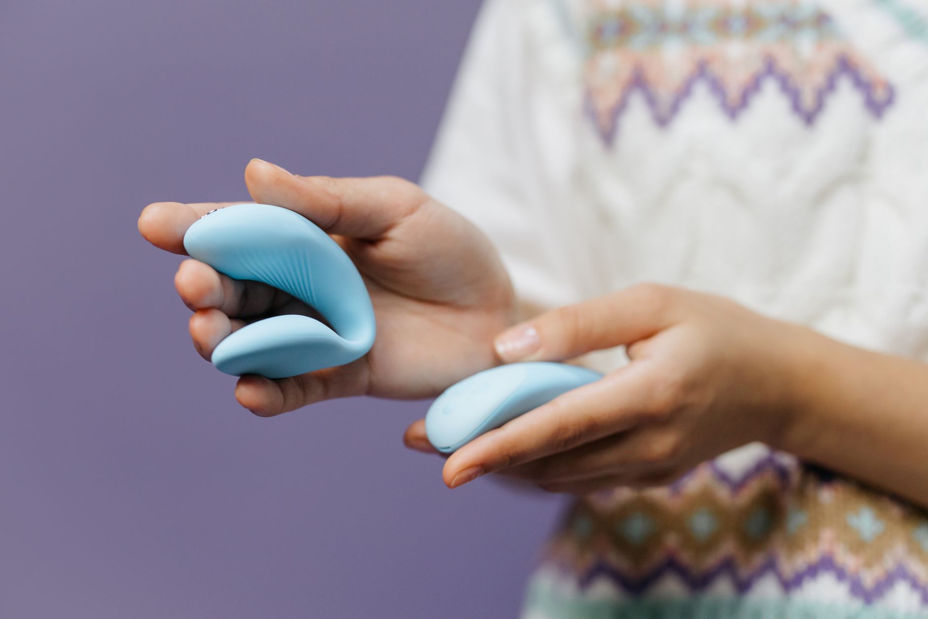 Close-up of hands holding a sleek blue lemon vibrator against a soft background.