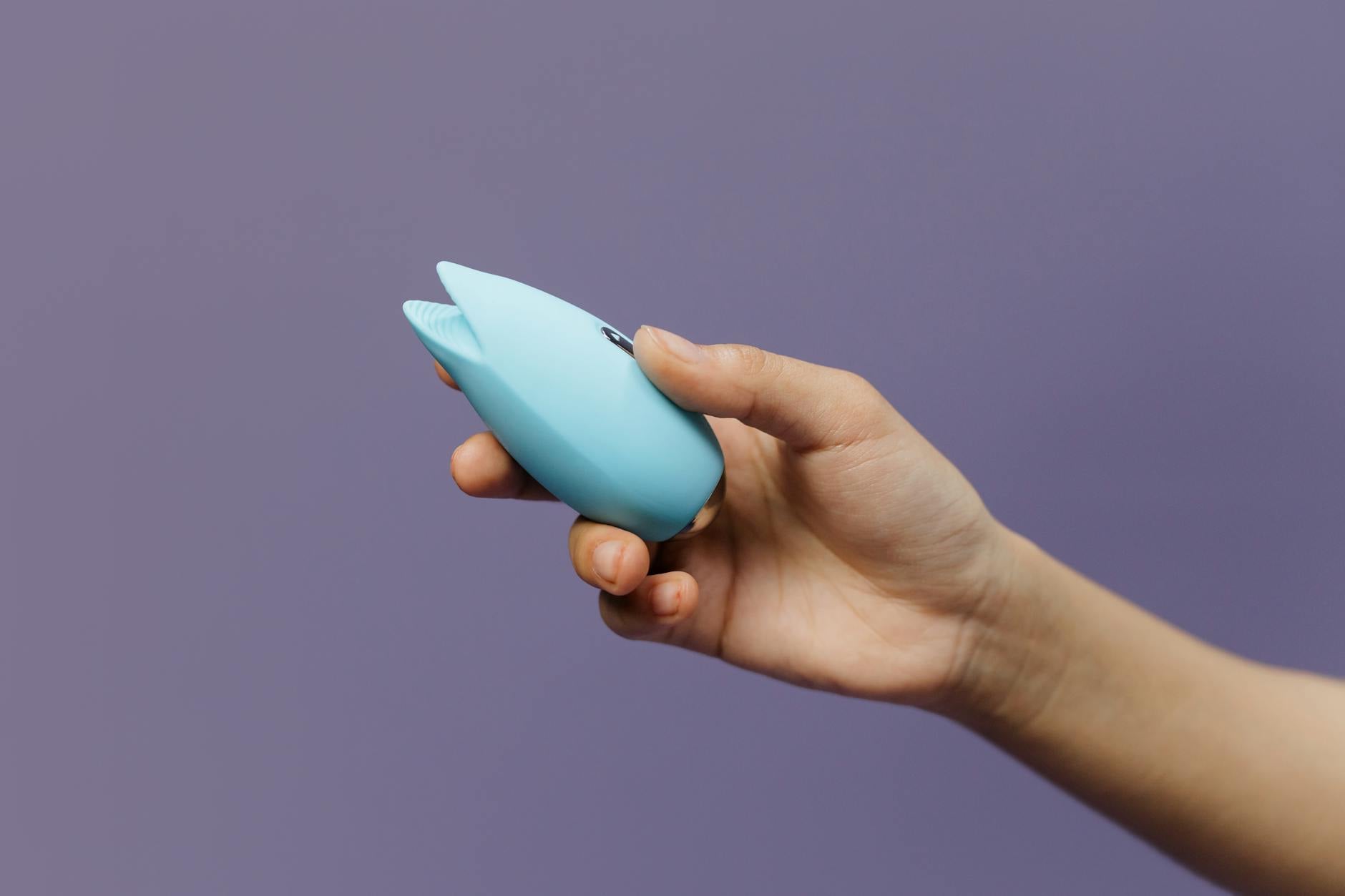 A woman holding two colorful vibrators against a purple background, symbolizing choice and self-directed pleasure.