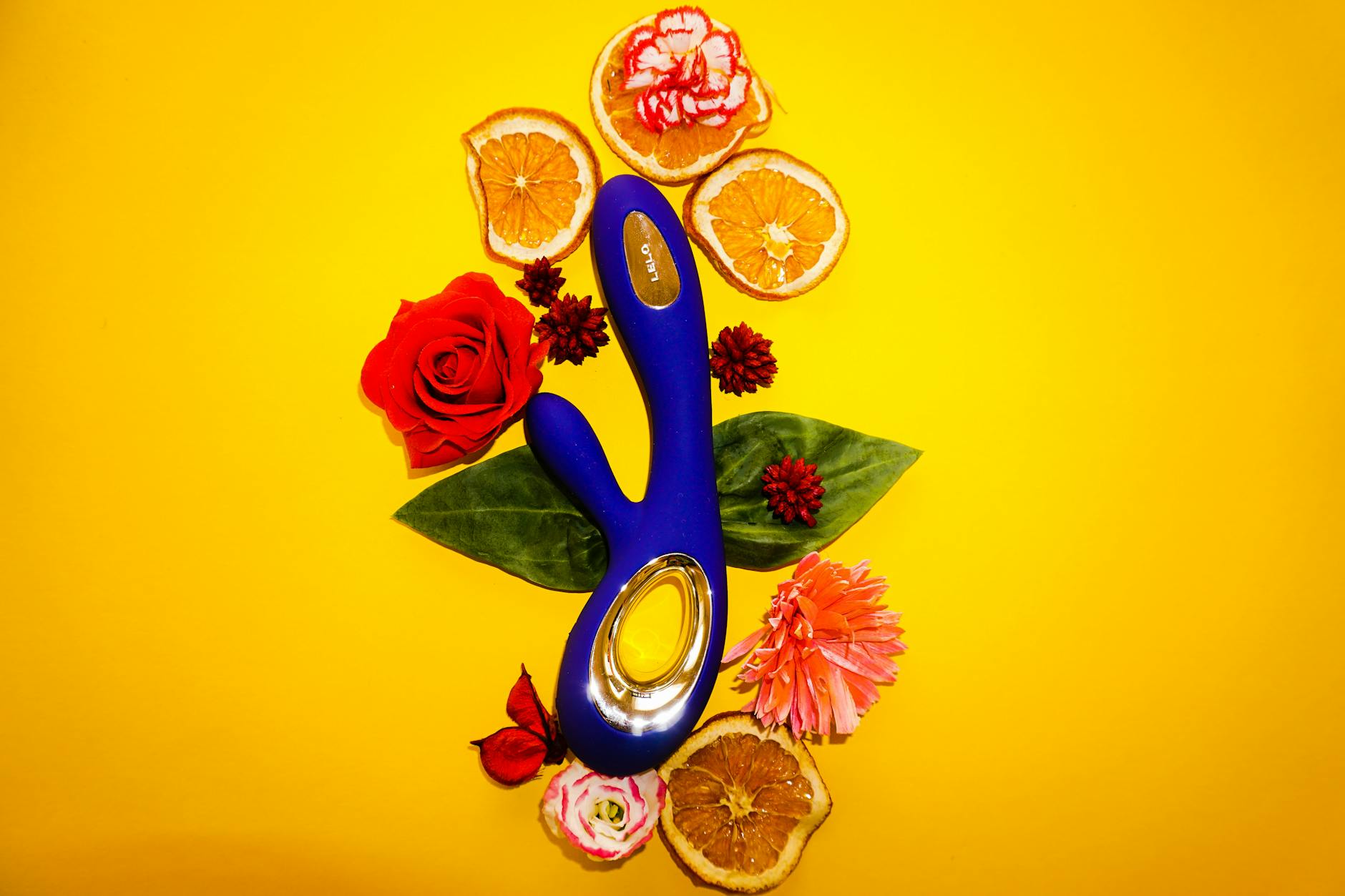 Bright lemon vibrator surrounded by citrus fruits and flowers on a vibrant yellow background