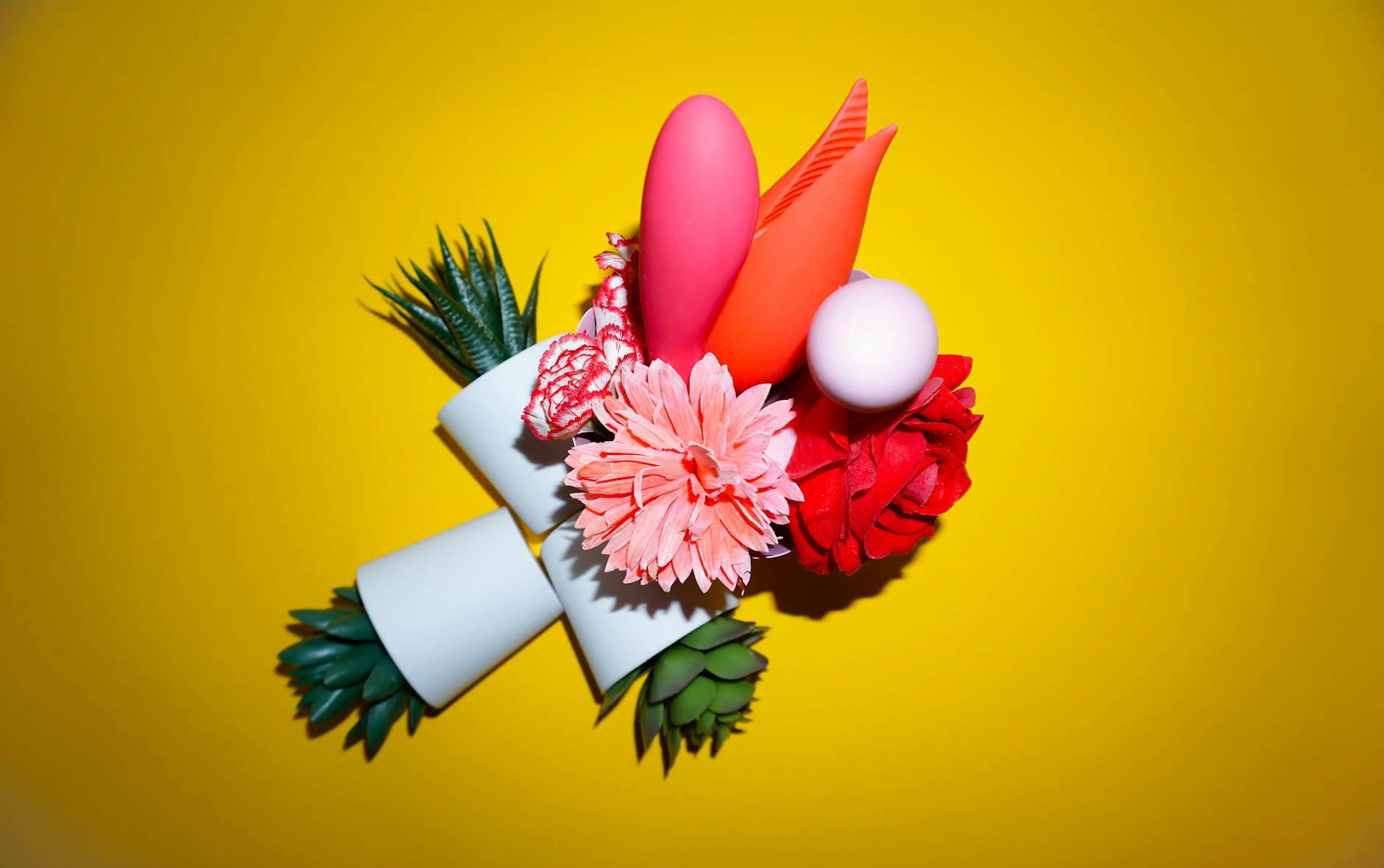 Colorful arrangement of vibrators and flowers on a bright yellow background representing solo pleasure exploration
