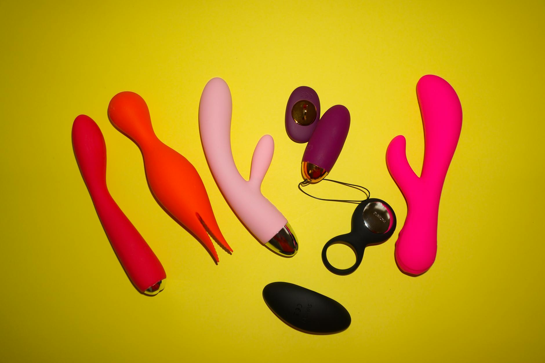 Colorful clitoral vibrators arranged on a bright yellow background, showcasing different shapes and styles