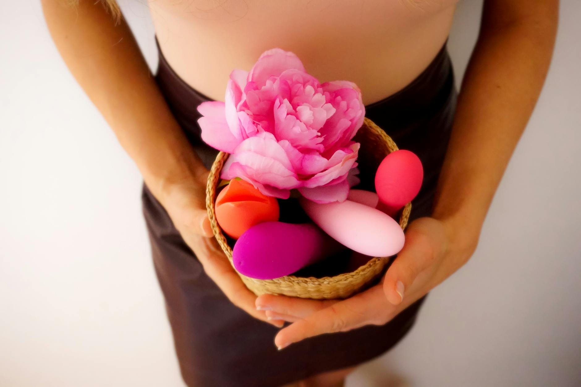 A person holding a basket containing colorful vibrators and a pink flower